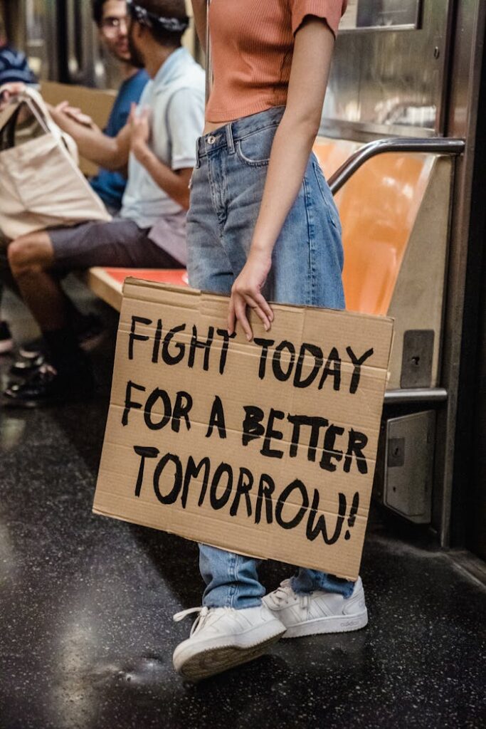 Woman holding sign 'Fight Today for a Better Tomorrow' on subway train.